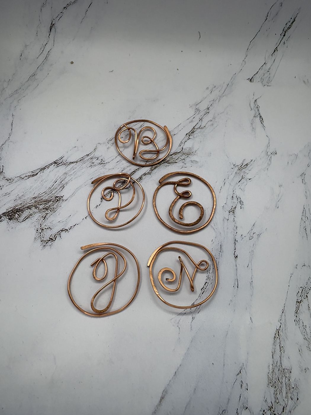 Hammered copper initial bookmarks laid out on marble